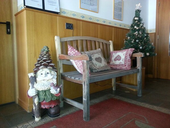 Un banco de madera con almohadones decorativos, un pequeño árbol de Navidad y una figura de gnomo en un pasillo.