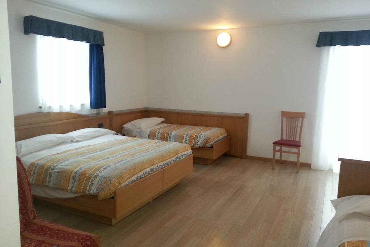 Una habitación con dos camas de madera, una silla y una lámpara fijada a la pared.