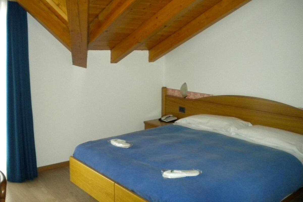 Una cama individual con cabecera de madera, una mesita de noche con un teléfono y una colcha azul.