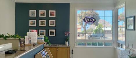 Un área de recepción con mostrador, cuadros enmarcados en la pared, una ventana con vistas al exterior y una zona de estar con una silla estampada.