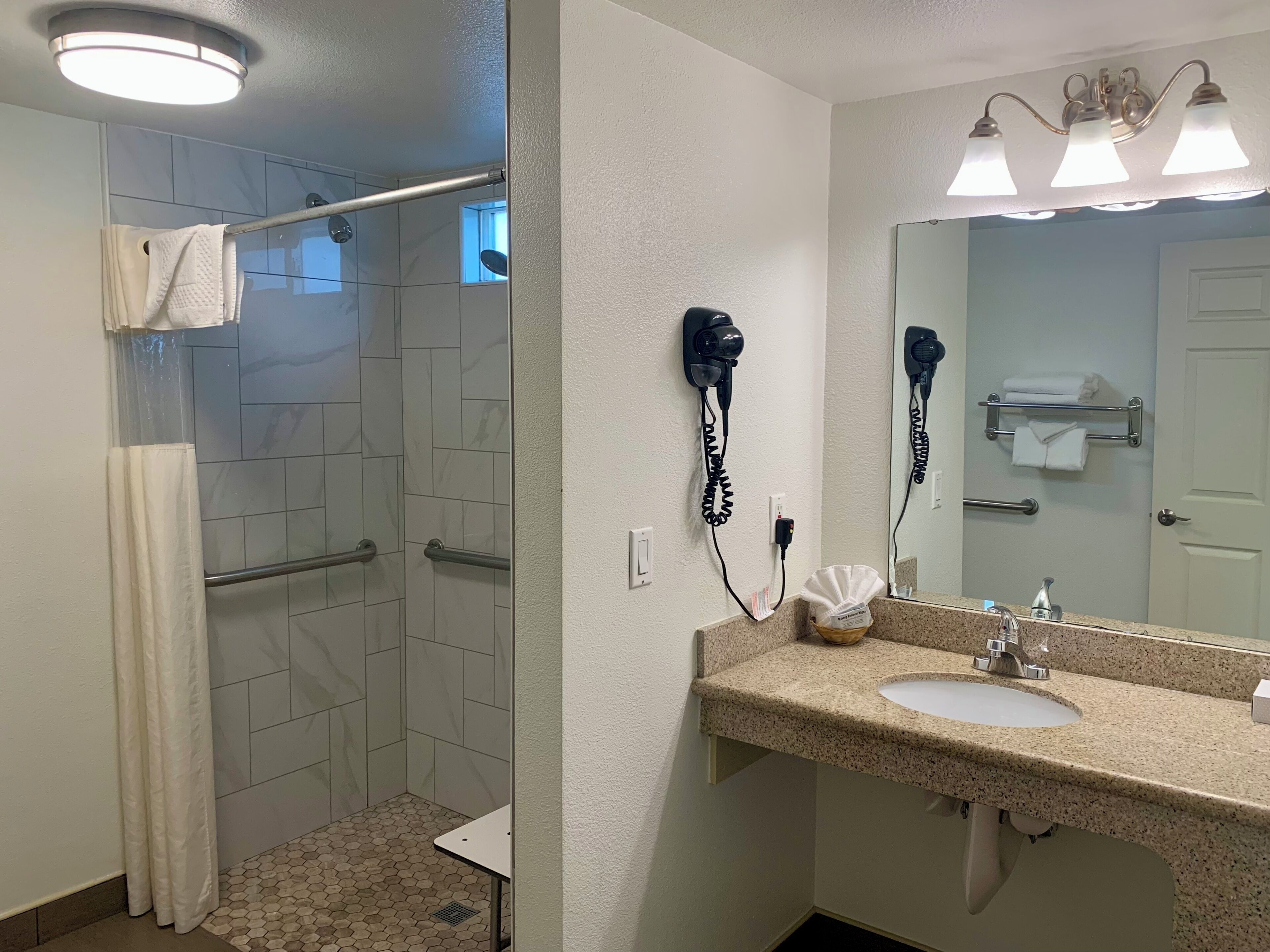 Casa de banho com chuveiro, lavatório e secadores de cabelo fixados na parede.
