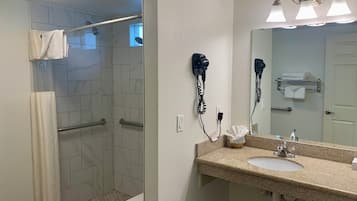Casa de banho com chuveiro, lavatório e secadores de cabelo fixados na parede.