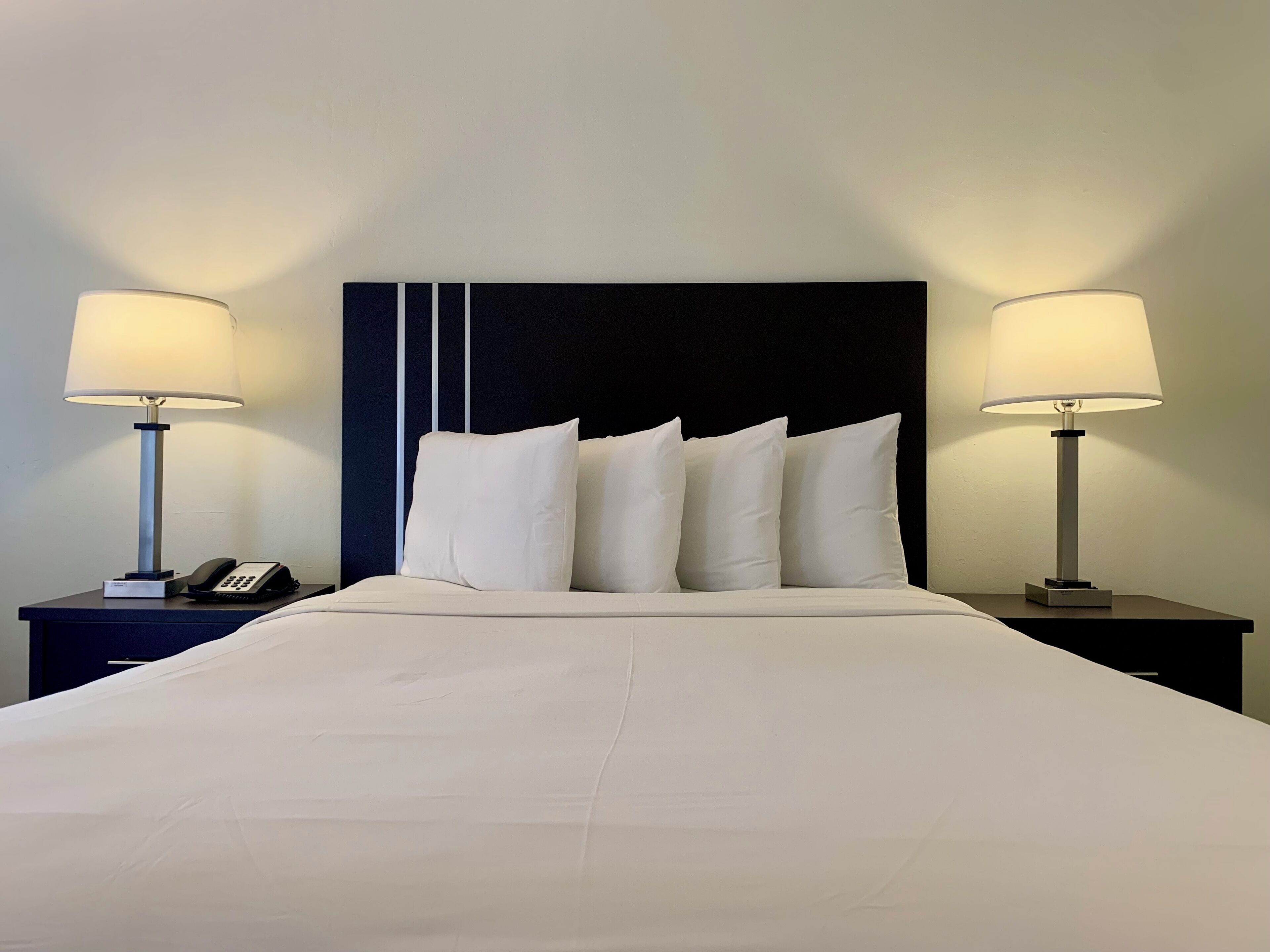 A neatly made bed with white linens and pillows, flanked by two bedside tables with lamps and a phone.