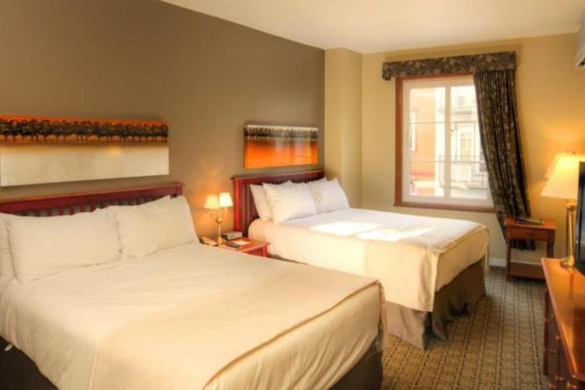 A hotel room with two beds, a television, and artwork on the walls.