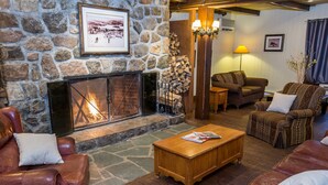 A cozy living room with a stone fireplace, leather sofas, and a wooden coffee table. - Place St-Bernard (Mont-Tremblant)