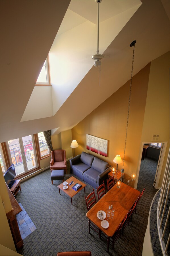 A spacious living area with a high ceiling, a dining table, a sofa, and a TV.