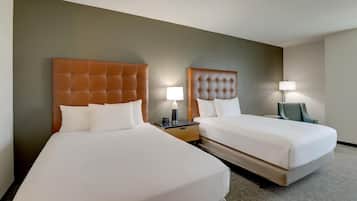 Habitación de hotel con dos camas, cada una con cabecero capitonado, ropa de cama blanca y lámparas de noche.