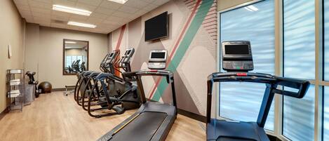 Un gimnasio con cintas de correr, elípticas y una bicicleta estática.