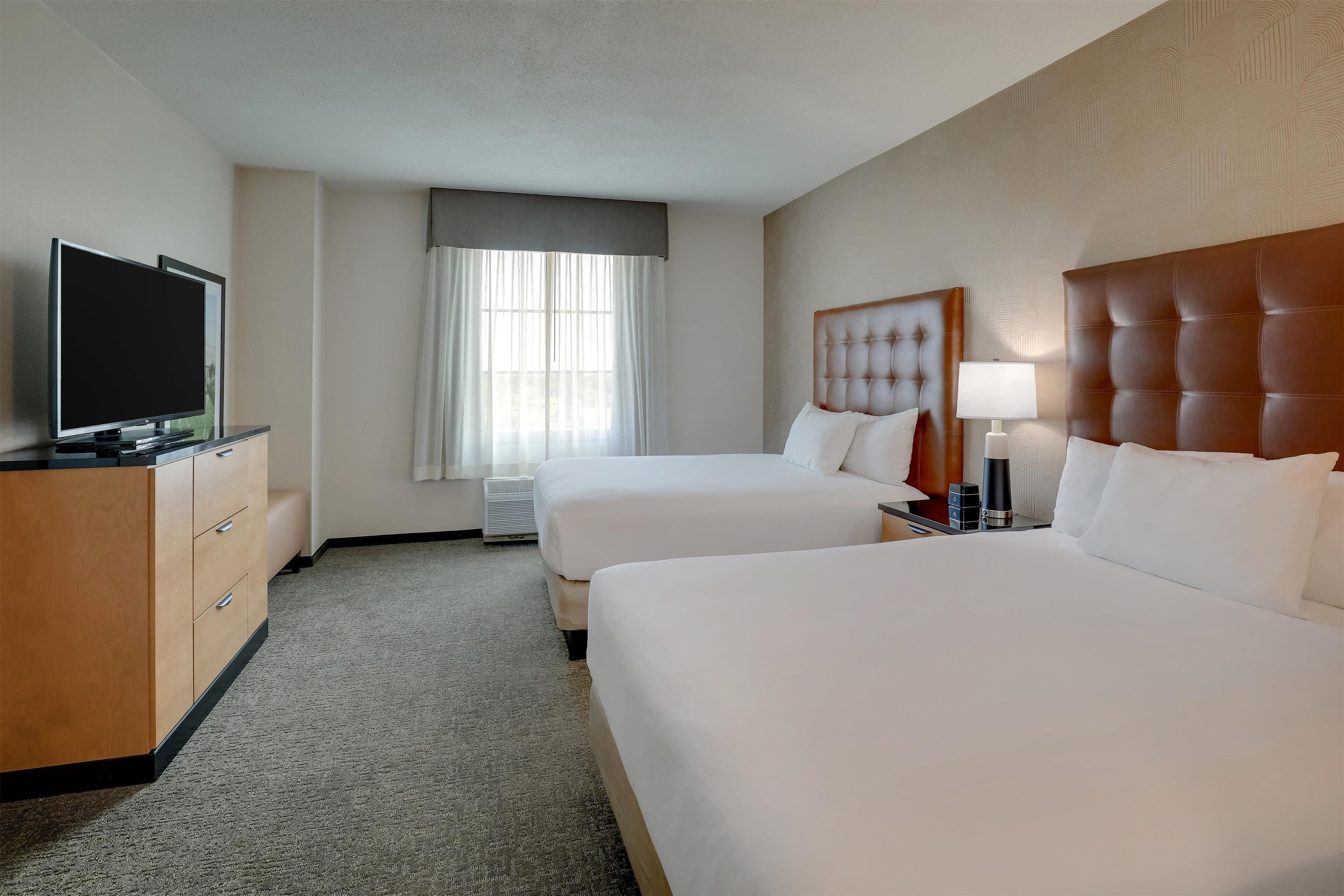 A hotel room with two beds, a TV, a desk with a lamp, and a window with curtains.