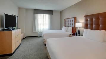 A hotel room with two beds, a TV, a desk with a lamp, and a window with curtains.