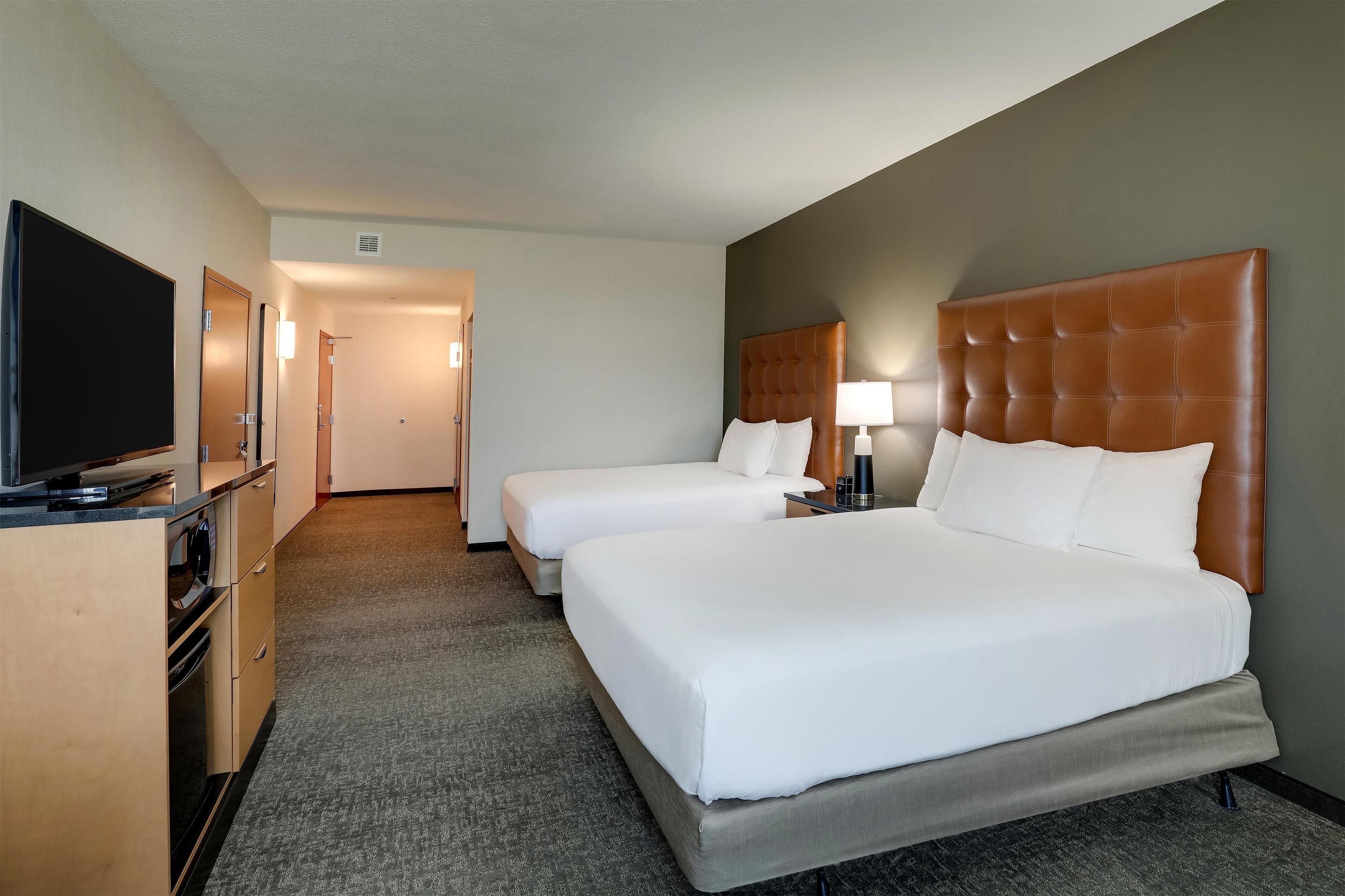 A hotel room with two beds, a TV, a desk, and a lamp.