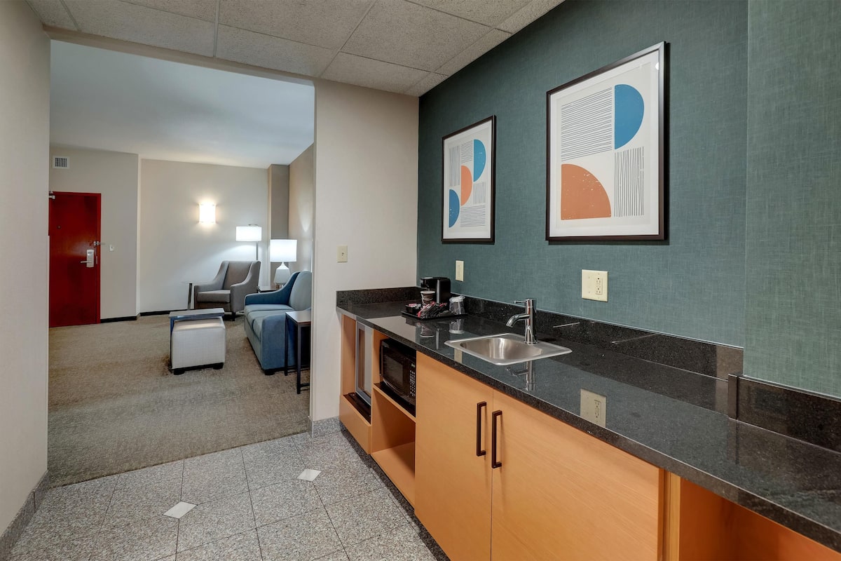 Eine moderne Küche mit Granit-Arbeitsplatten, einer Edelstahlspüle und Holzausbau. An der Wand befinden sich gerahmte abstrakte Kunstwerke, und im Schrank ist eine Mikrowelle zu sehen.