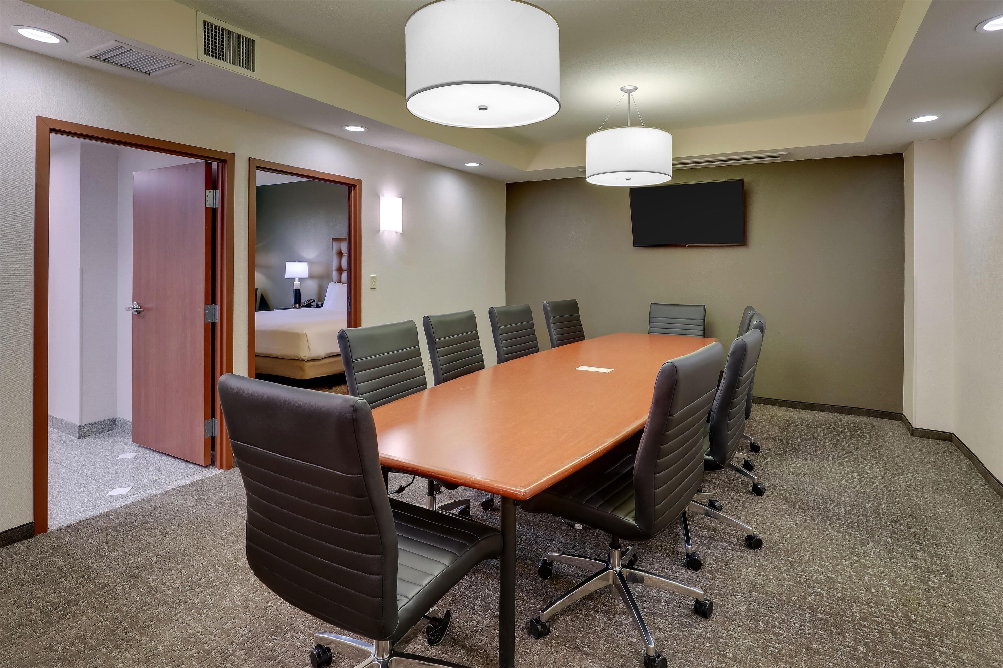 Une salle de conférence avec une table en bois, des chaises noires et un grand luminaire blanc au plafond.