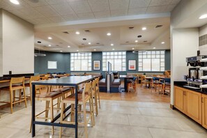 A spacious dining area with multiple tables and chairs, large windows, and a kitchen area with appliances. - Drury Inn & Suites Dayton North (Dayton)