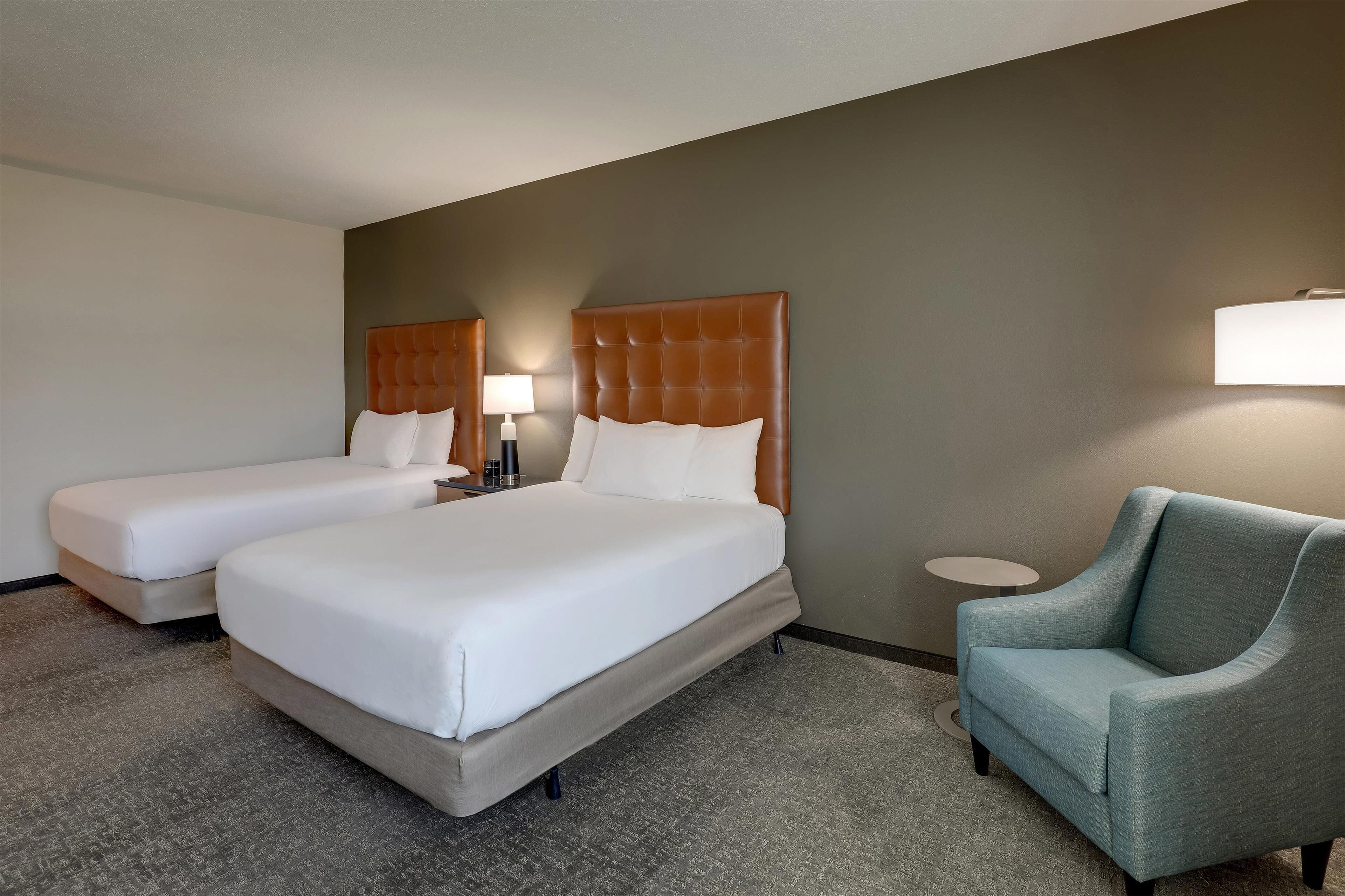 Une chambre d’hôtel avec deux lits, une chaise, une lampe et une petite table.