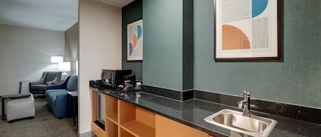 Una cocina moderna con encimera negra, pileta de acero inoxidable y armarios de madera. Hay dos obras de arte abstracto enmarcadas en la pared.