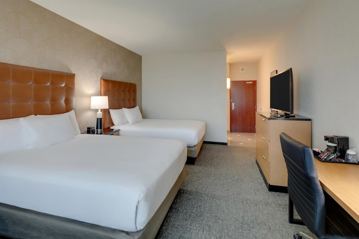 Ein Hotelzimmer mit zwei Betten, einem Schreibtisch, einem Fernseher und einem Kleiderschrank.