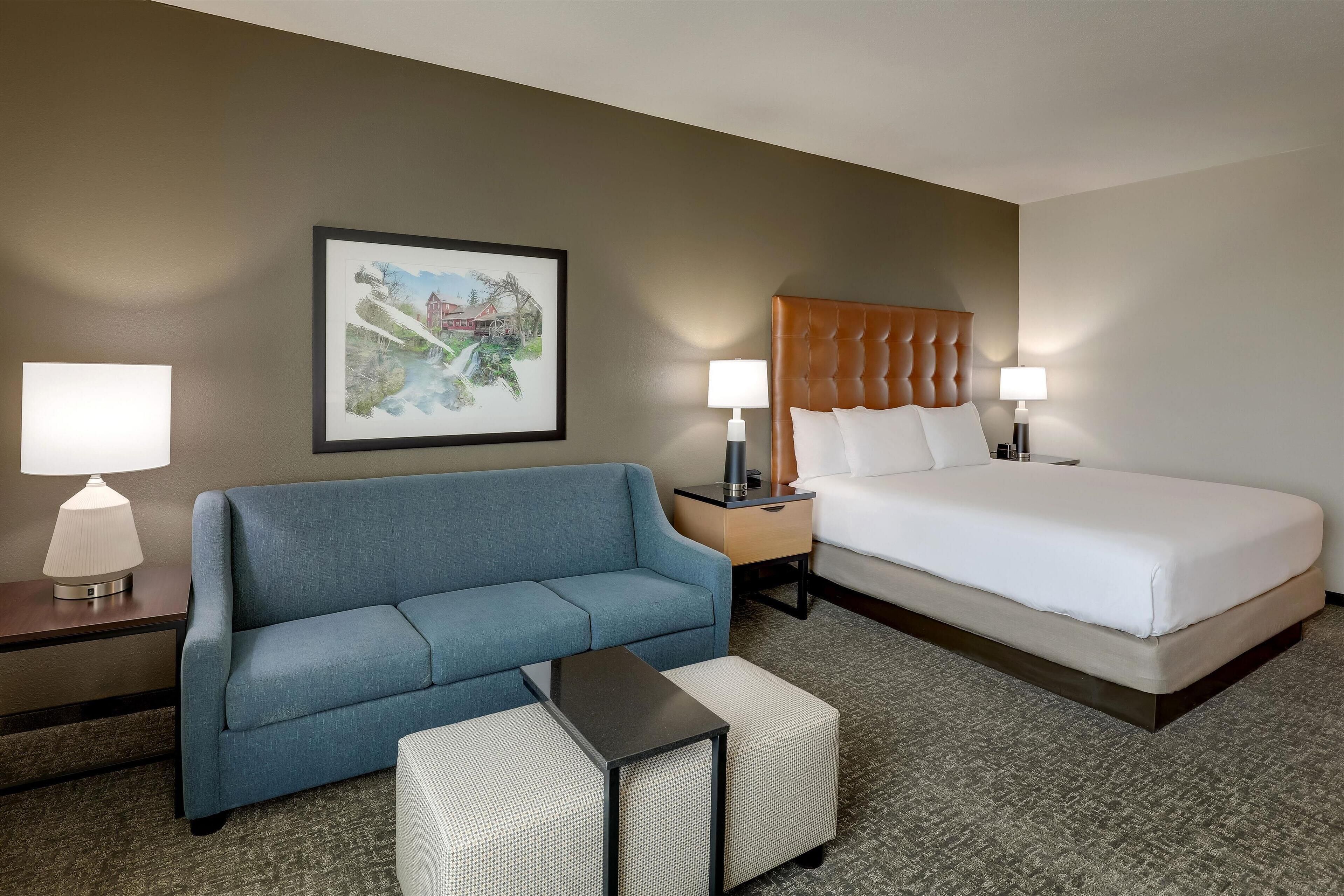 A hotel room with a bed, a blue sofa, a small table, two bedside lamps, and a framed picture on the wall.