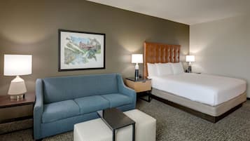 A hotel room with a bed, a blue sofa, a small table, two bedside lamps, and a framed picture on the wall.