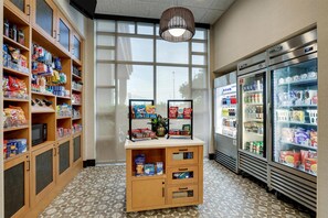 A snack and beverage kiosk with shelves stocked with various snacks and drinks, a microwave, and a refrigerator. - Drury Inn & Suites Montgomery (Montgomery)