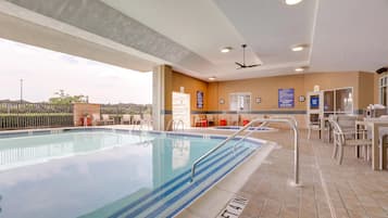 A swimming pool with a tiled deck, a ceiling fan, and a view of the surrounding area.