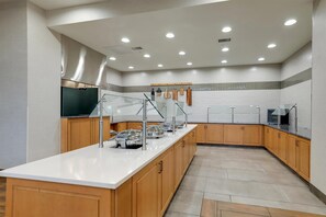 A modern kitchen with a long counter, wooden cabinets, and stainless steel appliances.