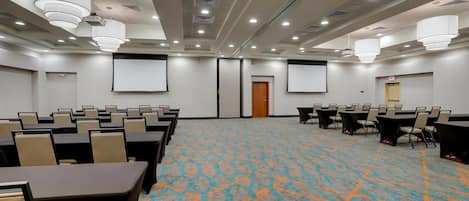A conference room with a patterned carpet, multiple tables, chairs, and a projector screen.