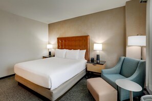 A hotel room with a large bed, two bedside tables with lamps, a blue armchair, and a small round table. - Drury Inn & Suites Montgomery (Montgomery)