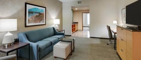 A hotel room with a blue sofa, a small table with a lamp, a television, and a cabinet.