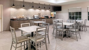 A modern dining area with multiple tables and chairs, a kitchen counter with appliances, and a flat-screen TV mounted on the wall. - La Quinta Inn & Suites by Wyndham Fredericksburg (Fredericksburg)