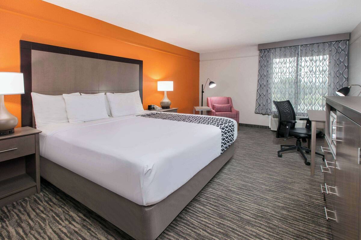 Una habitación de hotel con una cama grande, un escritorio, una silla, una lámpara y un armario.