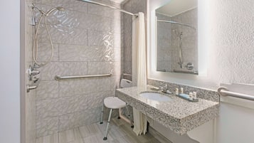 A bathroom with a shower, grab bar, and a sink with a mirror.