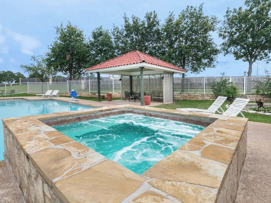 Ein Schwimmbecken mit Whirlpool, Liegestühlen und einem Pavillon.