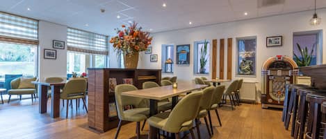 Un restaurante con piso de madera, sillas verdes, una mesa central y un jarrón decorativo con flores.