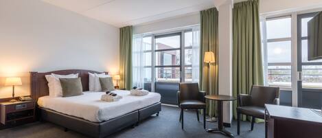 A hotel room with a bed, two chairs, a desk, and a window with curtains.