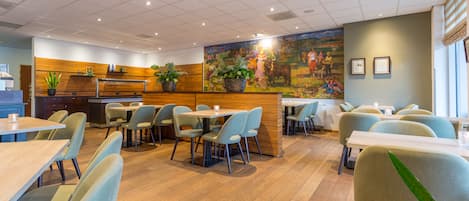 A modern restaurant with wooden flooring, light blue chairs, and a large mural on the wall.