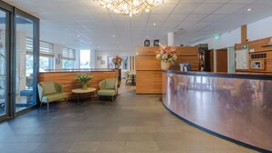 A reception area with a curved counter, two green armchairs, a small table with a vase of flowers, and a modern chandelier.