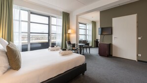 A hotel room with a large bed, a desk, a chair, a TV, and a wardrobe.