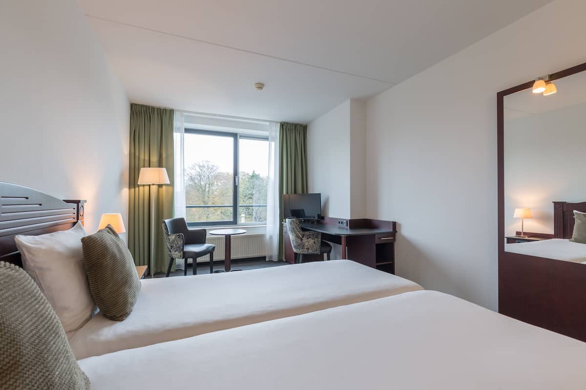 Une chambre d’hôtel avec un grand lit, un bureau, une chaise, une télévision et une fenêtre avec des rideaux.