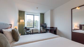 A hotel room with a large bed, a desk, a chair, a television, and a window with curtains.