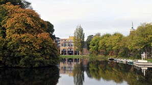 A riverside view with a building featuring multiple windows and a tower.