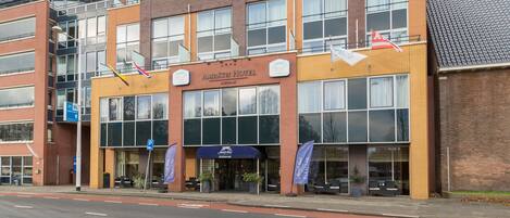 A hotel with a modern design, featuring a prominent entrance, multiple windows, and flags.