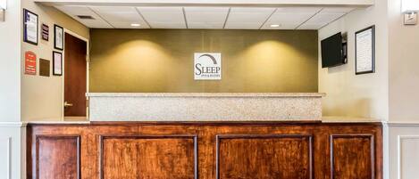 A reception area with a wooden reception desk, a 'Welcome' mat, and a sign for 'Sleep Inn & Suites'.