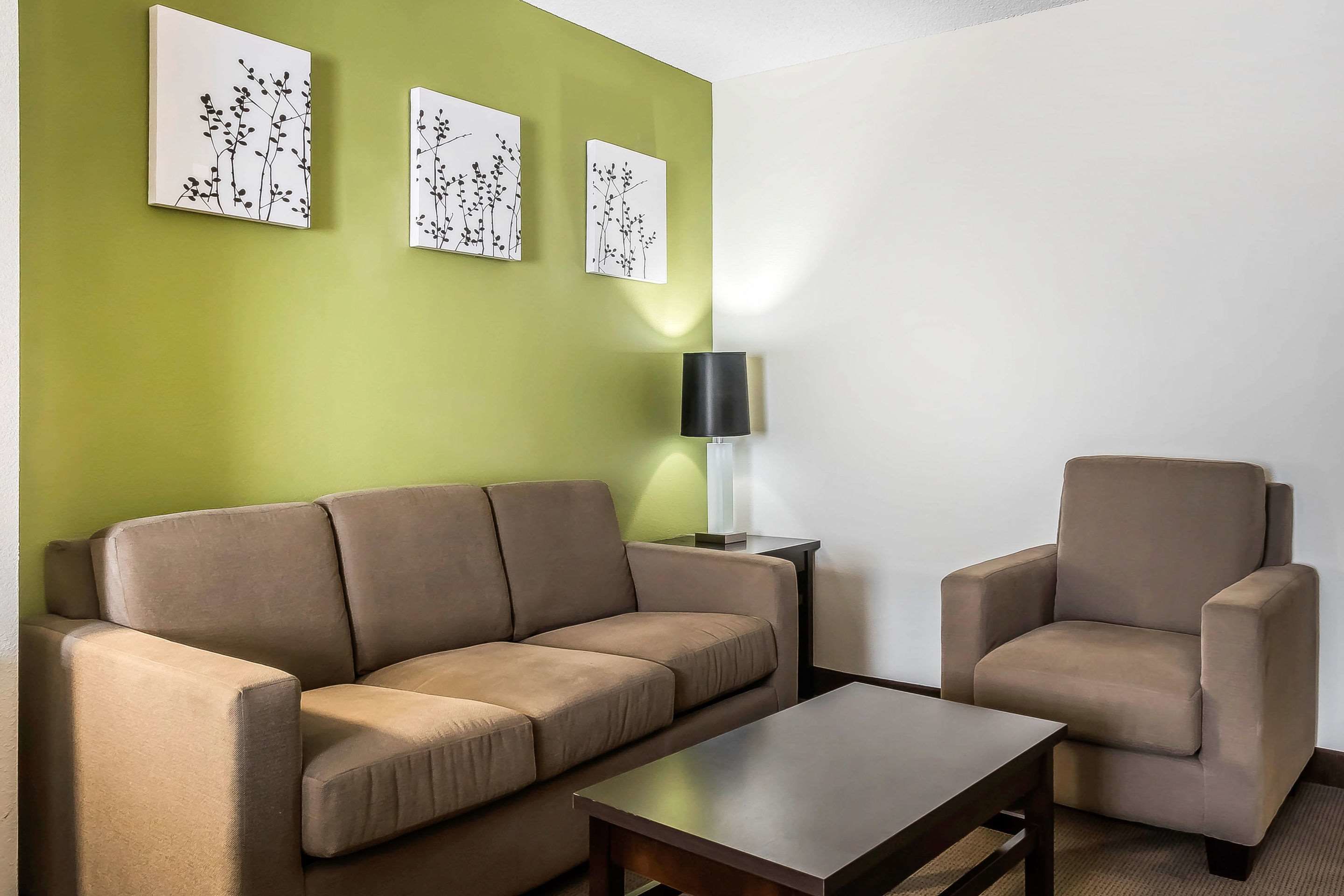 A living room with a beige sofa, a matching armchair, a coffee table, and three wall-mounted artworks.