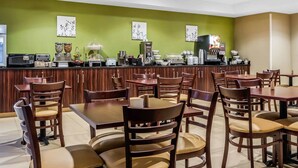 Un restaurant avec des tables et des chaises en bois, un comptoir avec des machines à café et des œuvres d’art mural.