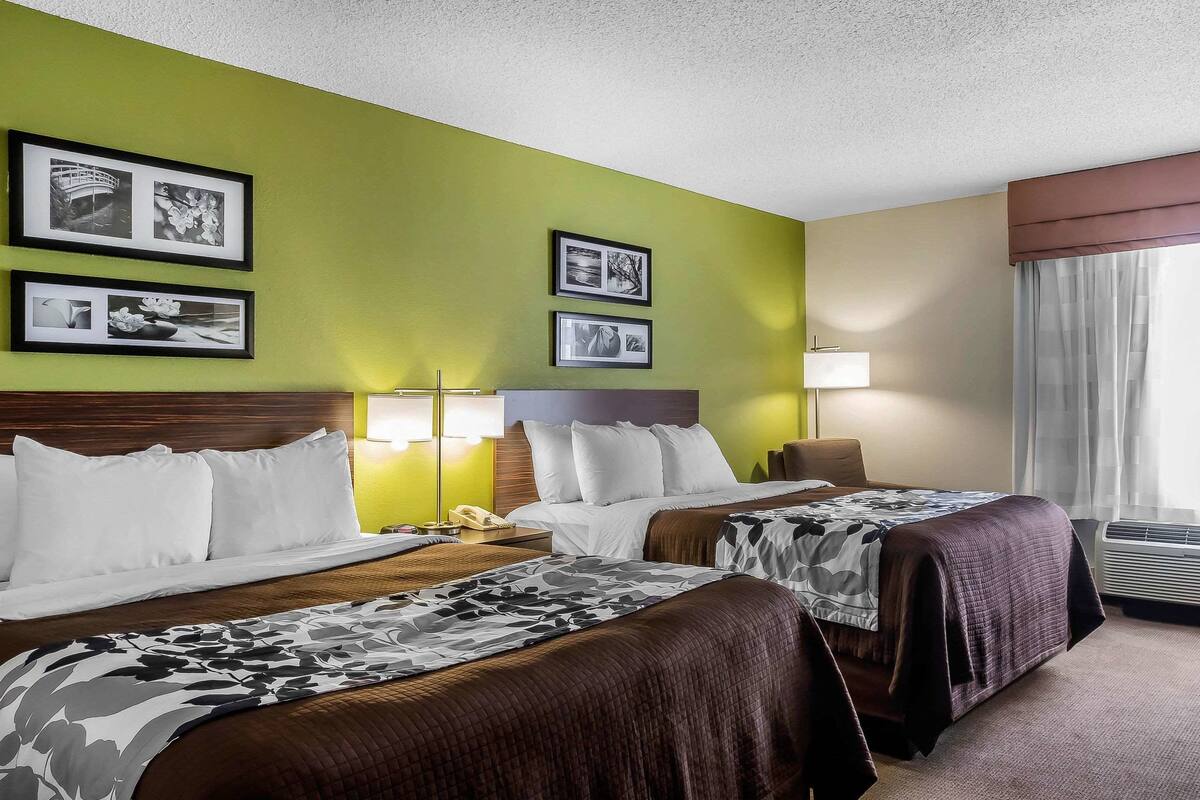 A hotel room with two beds, a wooden headboard, a green wall, and framed pictures.