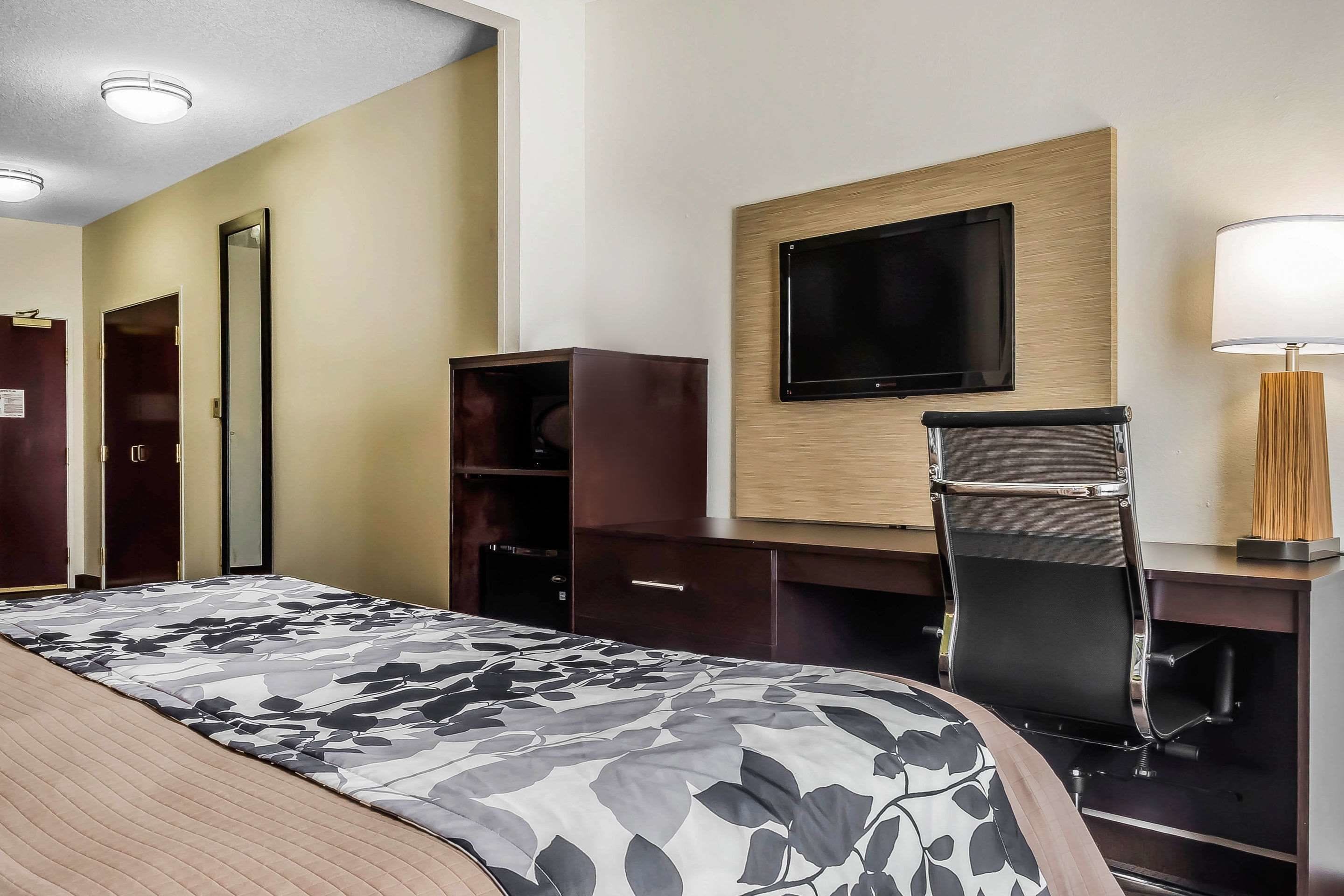 Une chambre d’hôtel comprenant un lit, un bureau avec une chaise, un téléviseur fixé au mur et une lampe.