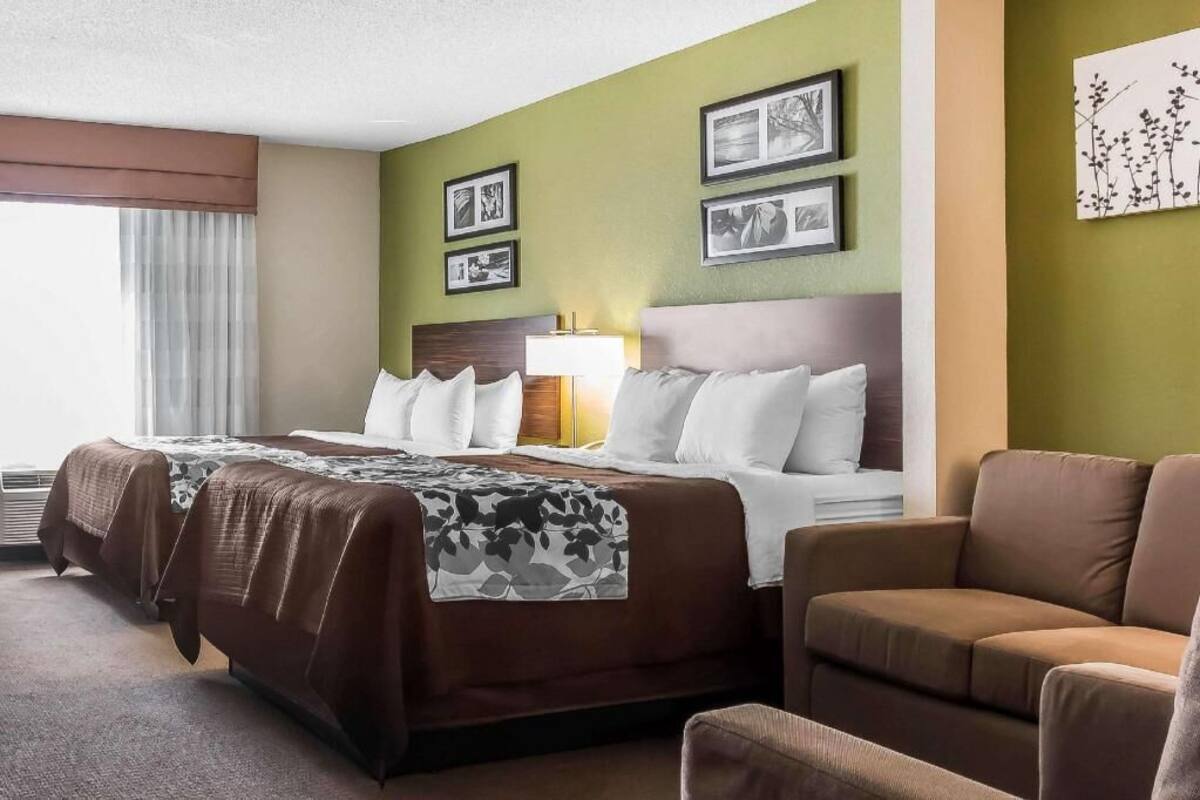 A hotel room with a large bed, a sofa, a desk, and a lamp.