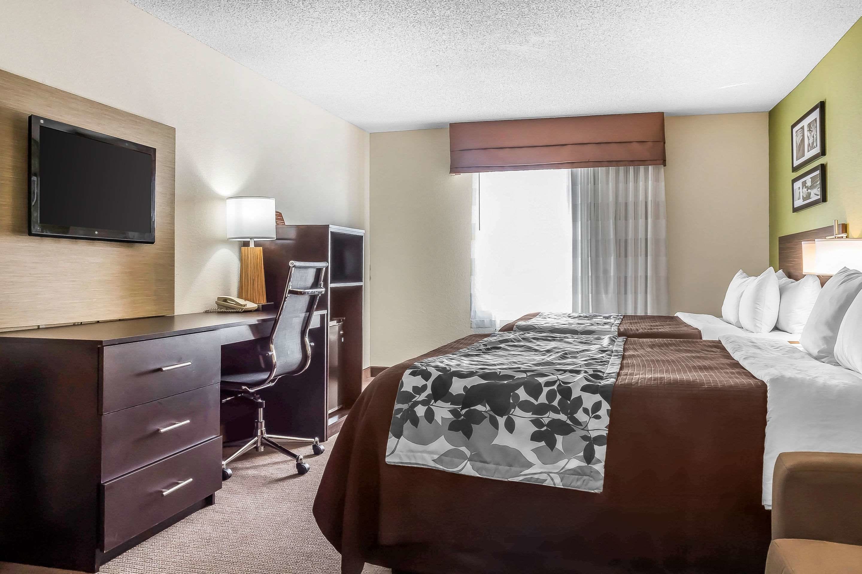 Een hotelkamer met een bed, bureau, stoel, televisie en raam met gordijnen.