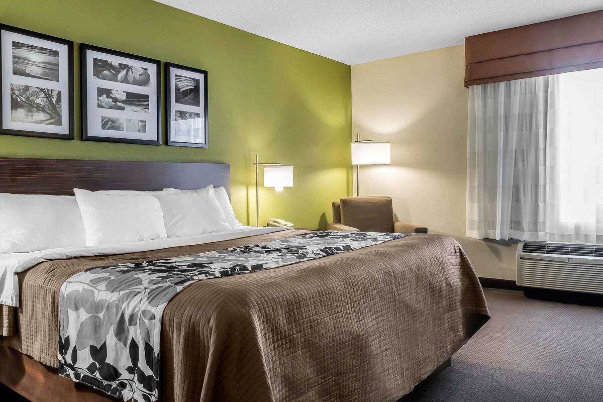 A hotel room with a large bed, a chair, a desk, and a window with curtains.